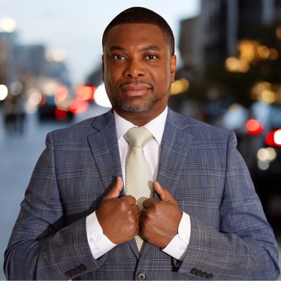 Bryan Starks, Founder and CEO of Starks Technology Services, in a blue plaid suit against a city backdrop at dusk